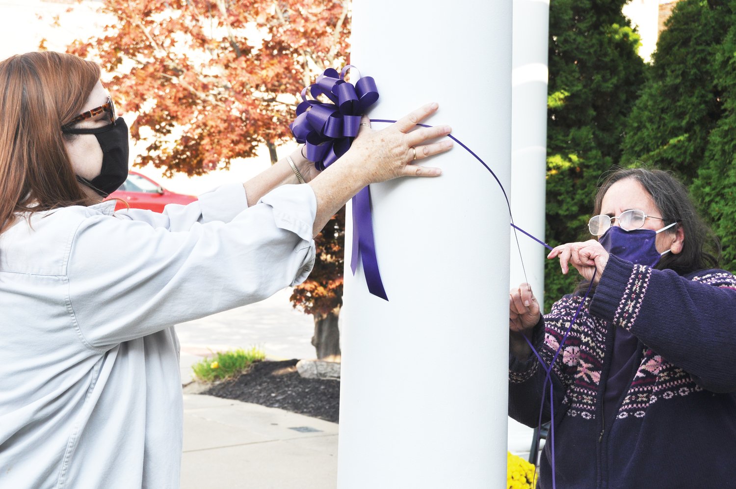 Deb Lee, left, and Kathy Walker, employees of the Family Crisis Shelter, tie a purple ribbon representing domestic violence awareness at Marie Canine Plaza Tuesday. October is Domestic Violence Awareness Month.